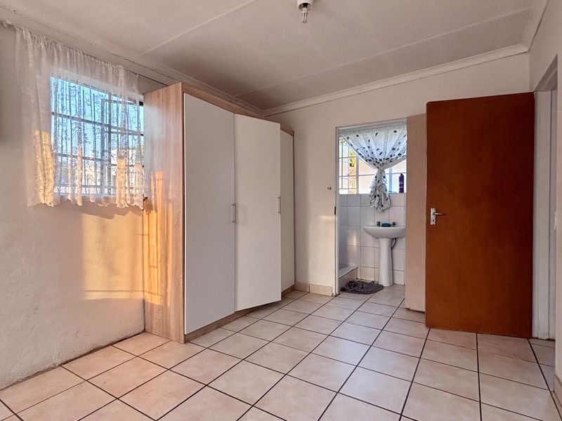 A bedroom featuring tiled flooring, a built-in wardrobe, and an attached en-suite area with a pedestal basin.