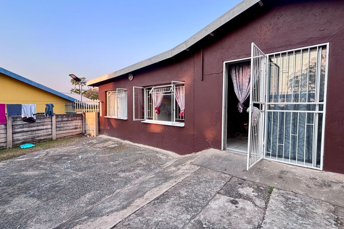 Rear exterior view of the house featuring a concrete paved yard, security gate, and burglar bars on the windows.