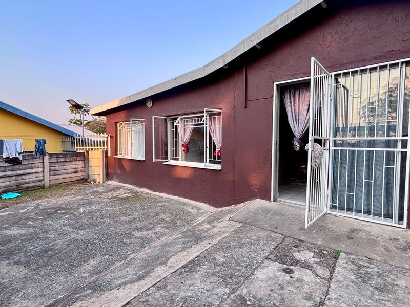 Rear exterior view of the house featuring a concrete paved yard, security gate, and burglar bars on the windows.