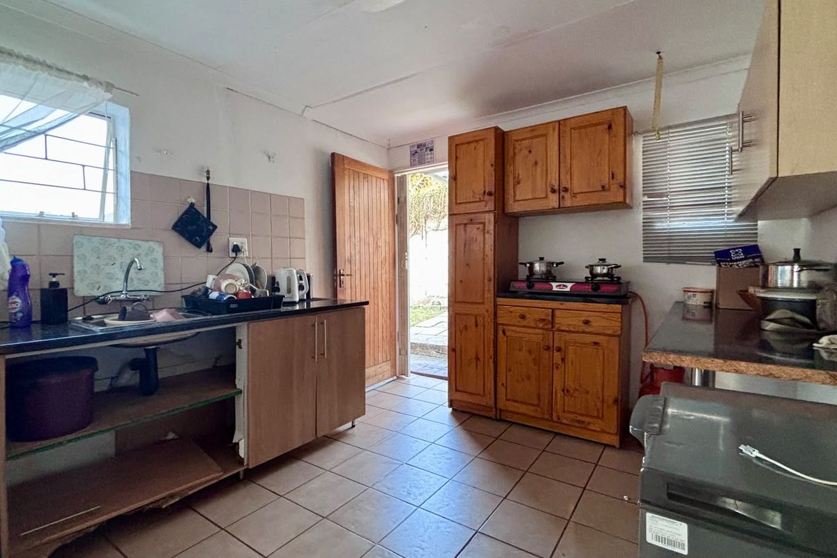 A functional kitchen featuring wooden cabinetry, tiled flooring, and a tiled backsplash, with direct access to the exterior.