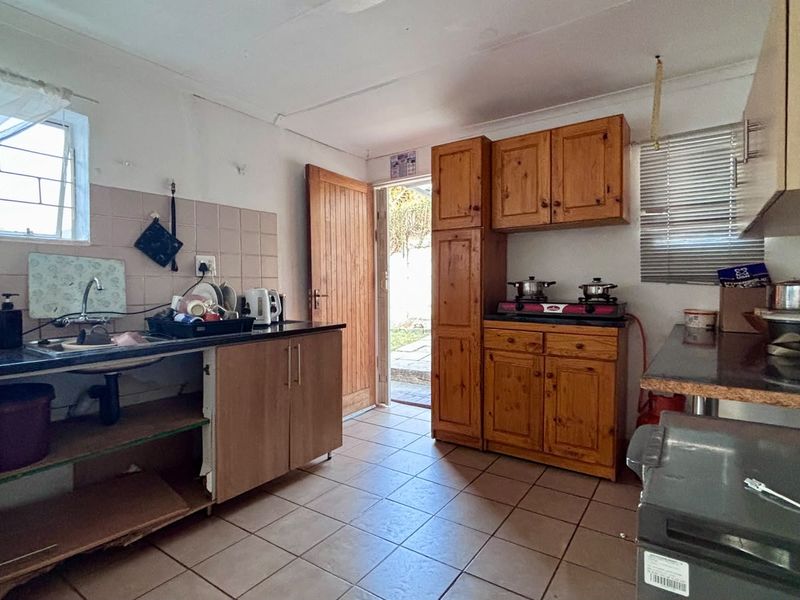 A functional kitchen featuring wooden cabinetry, tiled flooring, and a tiled backsplash, with direct access to the exterior.