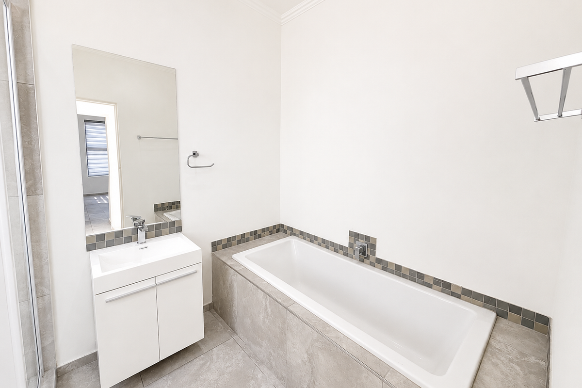 A clean, modern bathroom featuring a built-in vanity with basin, a tiled bathtub surround, and neutral wall finishes.