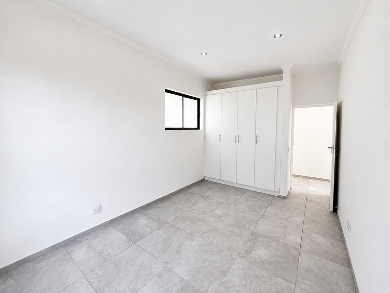 A bright, empty bedroom featuring neutral tiled flooring, built-in cupboards, and recessed downlighting, offering a clean and modern blank canvas.
