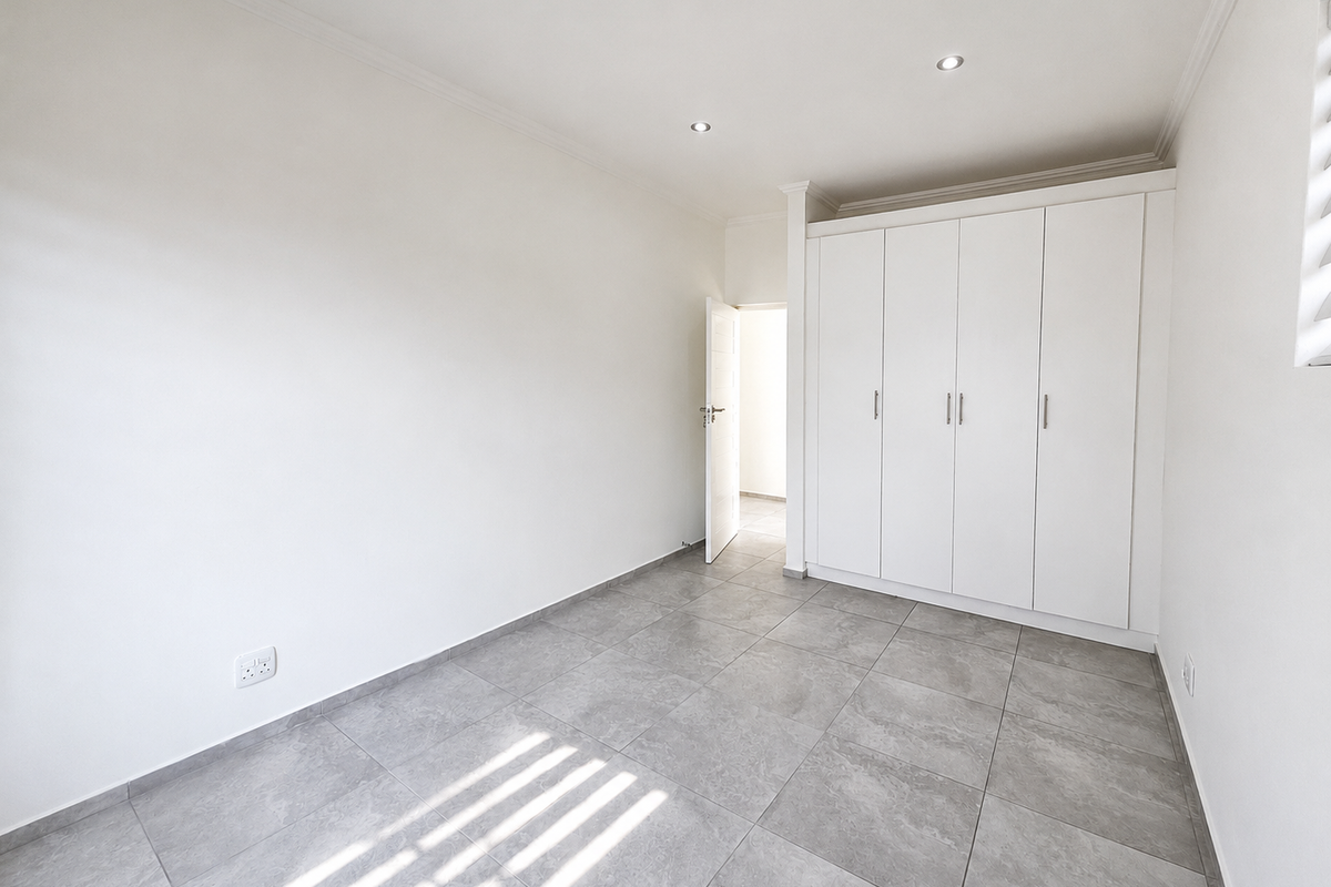 A bright, empty bedroom featuring modern grey floor tiles, built-in white cupboards, and recessed ceiling lighting.