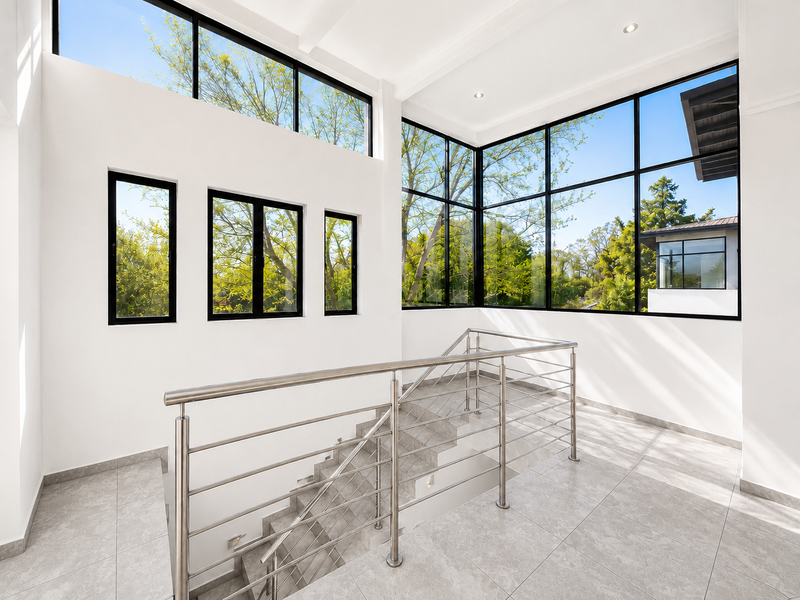 Bright and modern landing area featuring a sleek stainless steel balustrade, large black-framed windows, and neutral tiled flooring with abundant natural light.