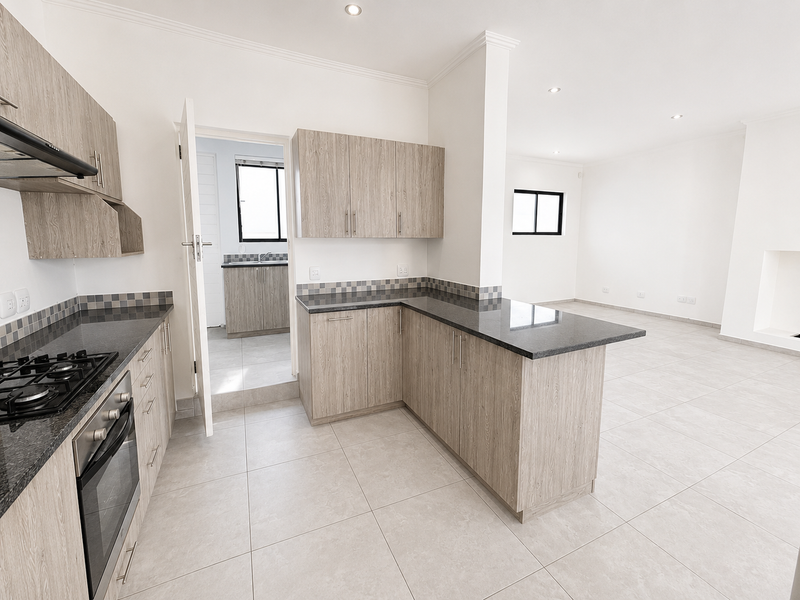 Modern open-plan kitchen featuring light wood cabinetry, granite countertops, built-in gas hob, and oven, flowing into a spacious, tiled living area.