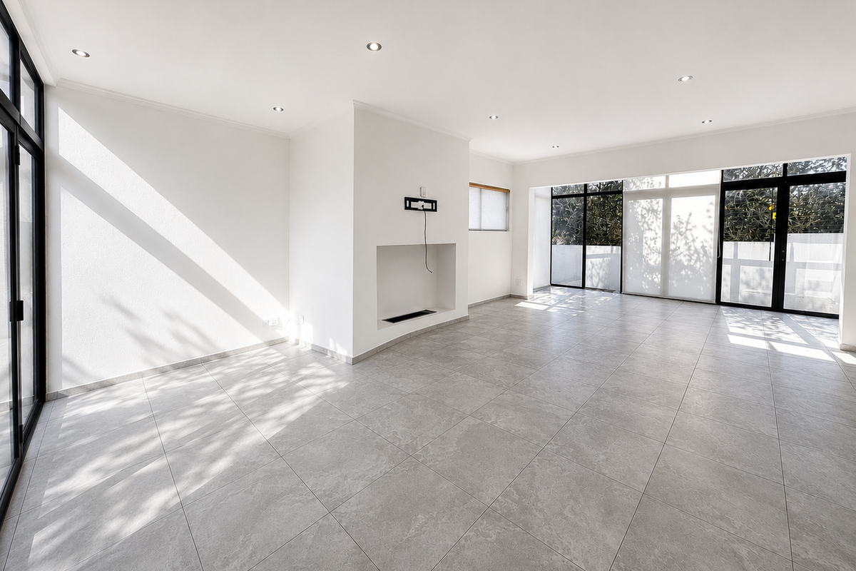 A bright, open-plan living area featuring neutral tiled flooring, recessed lighting, and large aluminium sliding doors leading to an outdoor space.