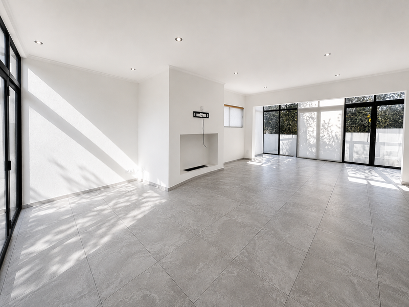 A bright, open-plan living area featuring neutral tiled flooring, recessed lighting, and large aluminium sliding doors leading to an outdoor space.