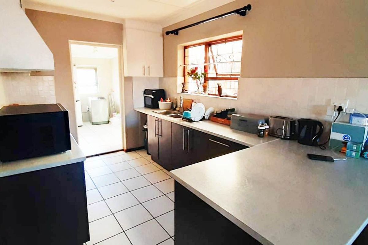 Functional kitchen featuring dark cabinetry, light countertops, tiled backsplash, and tiled flooring, with an adjacent utility area visible through the doorway.