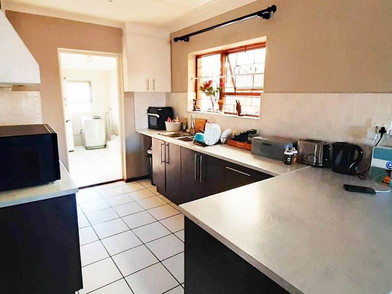 Functional kitchen featuring dark cabinetry, light countertops, tiled backsplash, and tiled flooring, with an adjacent utility area visible through the doorway.