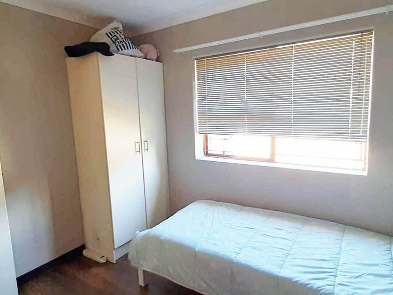 A functional bedroom featuring laminate flooring and window blinds, offering a neutral space ready for personalization.