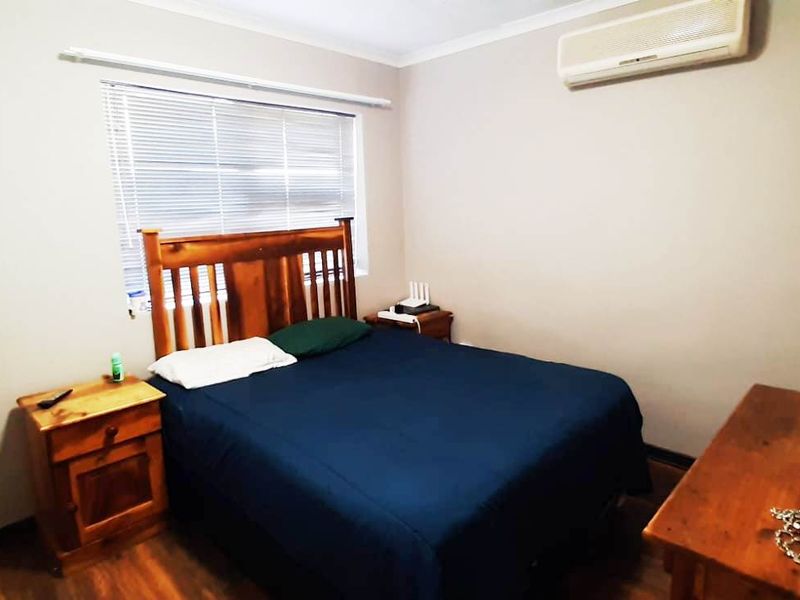 A functional bedroom featuring laminate flooring, a wall-mounted split-system air conditioner, and venetian blinds for privacy.