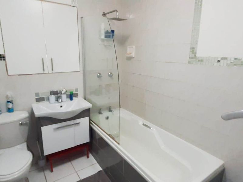 A functional bathroom featuring a shower-over-bath combination, a modern vanity unit, and a wall-mounted medicine cabinet with neutral tiled finishes.