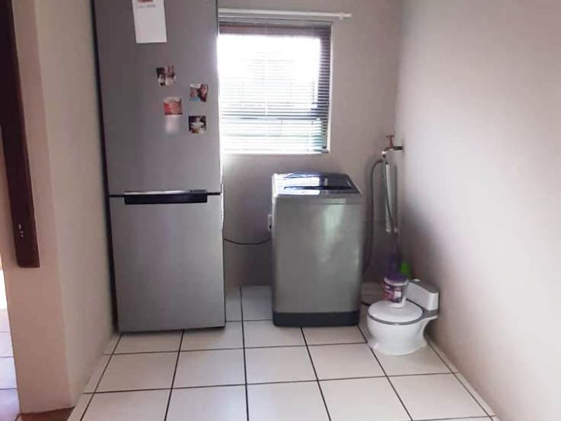 A functional laundry area featuring tiled flooring, plumbing connections for appliances, and a window providing natural light.