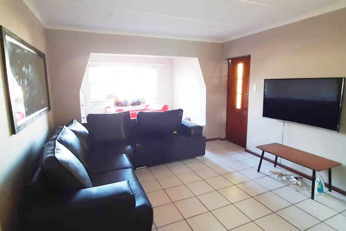 A living room featuring tiled flooring, a recessed window area, and a timber entrance door, providing a functional and neutral living space.