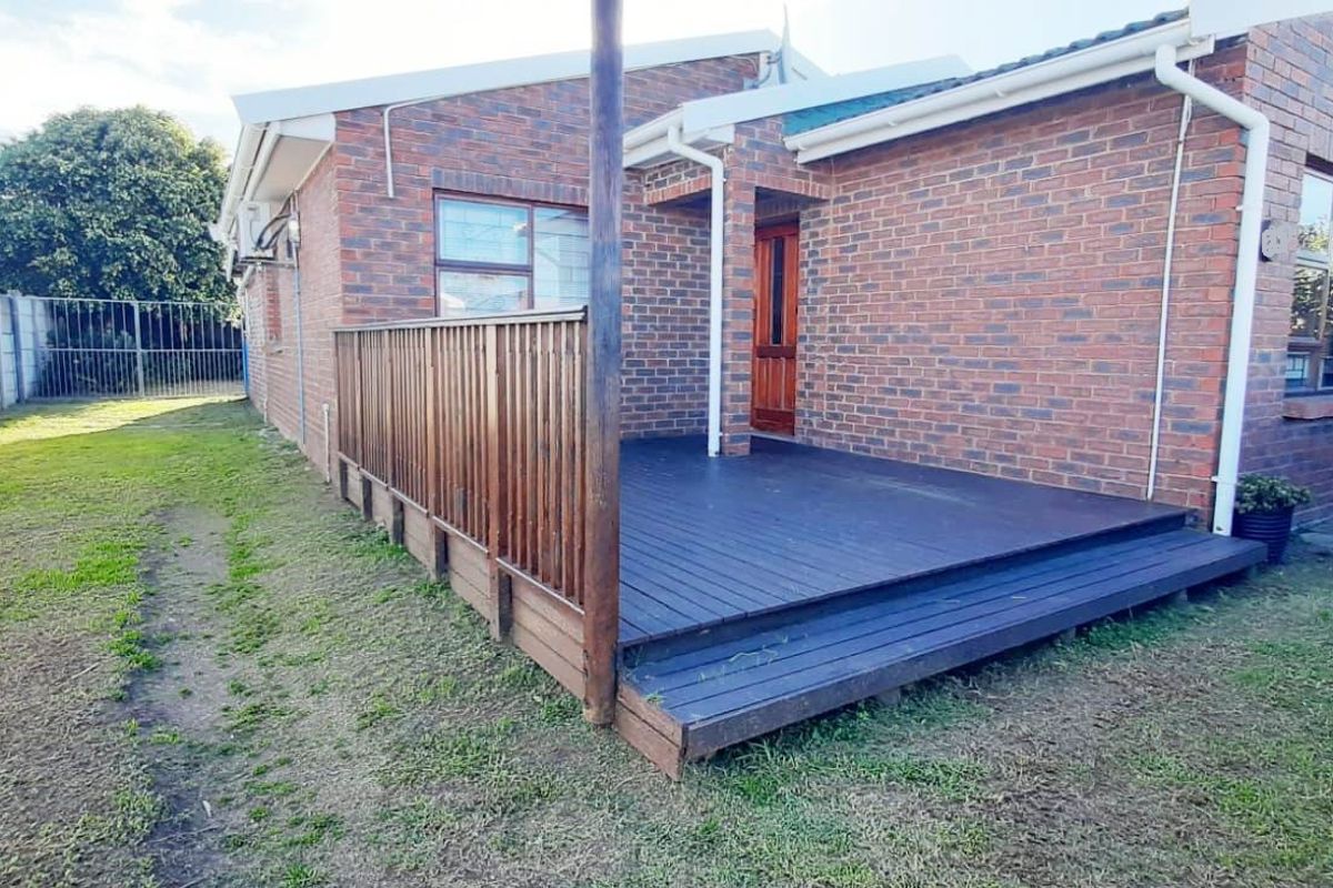 Rear view of the property featuring a raised timber deck, face brick exterior walls, and a private garden area with boundary walling.