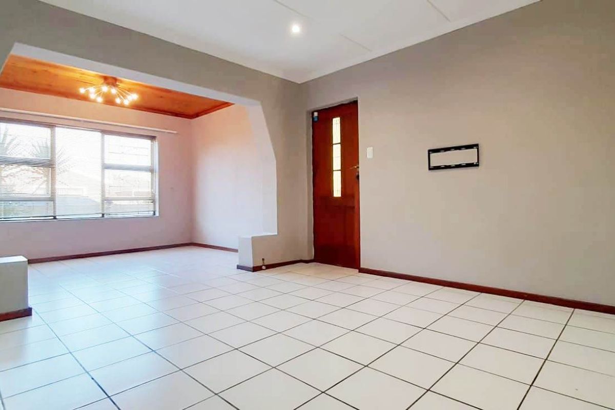 An empty, open-plan living area featuring neutral wall tones, tiled flooring, and a wooden entrance door with natural light.