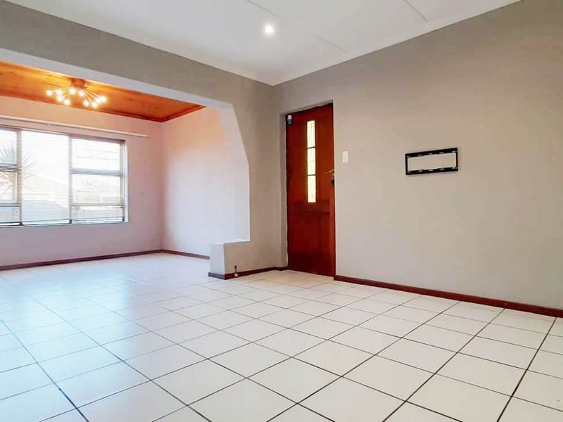 An empty, open-plan living area featuring neutral wall tones, tiled flooring, and a wooden entrance door with natural light.