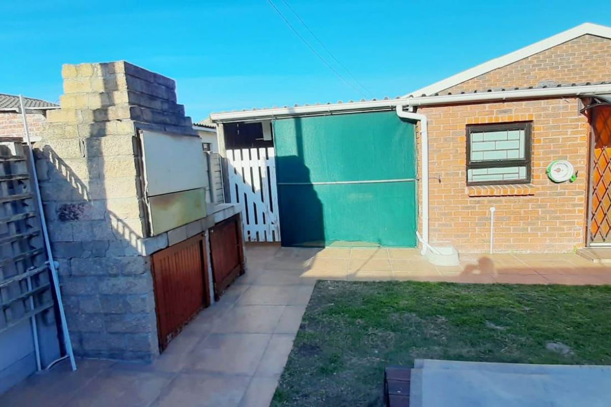 Rear exterior view featuring a built-in braai area, tiled patio space, and brick facade with security gate access.