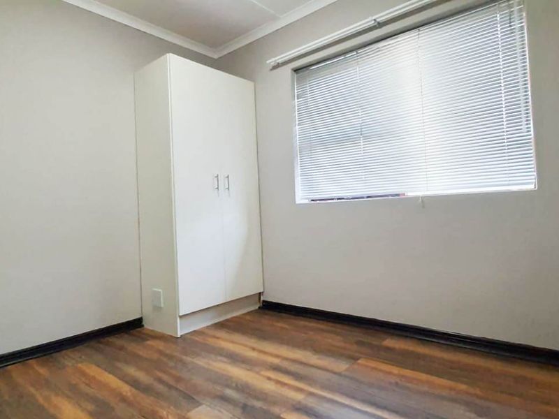 A clean, empty bedroom featuring durable laminate flooring, neutral wall tones, and a built-in wardrobe with fitted venetian blinds.