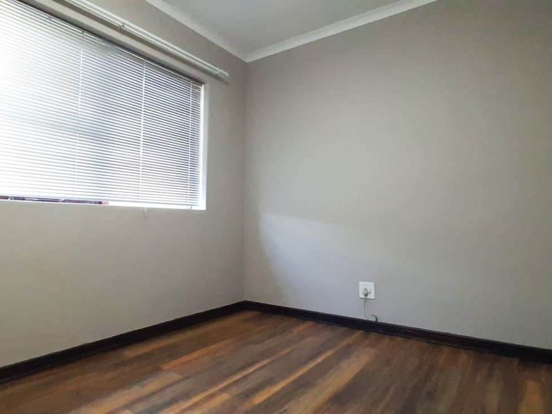 A clean, empty bedroom featuring laminate flooring, neutral wall tones, and fitted venetian blinds, offering a versatile space ready for personalization.