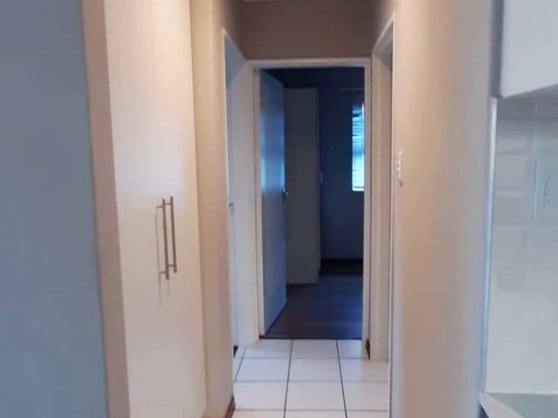 A clean, well-lit hallway featuring neutral wall tones, white tiled flooring, and built-in storage cabinetry, providing a seamless transition between living spaces.