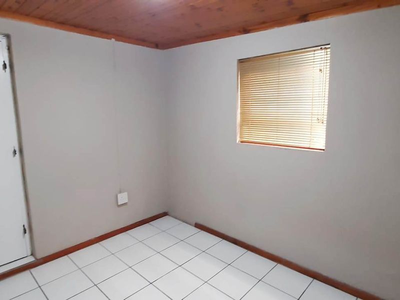 A simple, empty bedroom featuring tiled flooring, a timber ceiling, and a window fitted with venetian blinds.