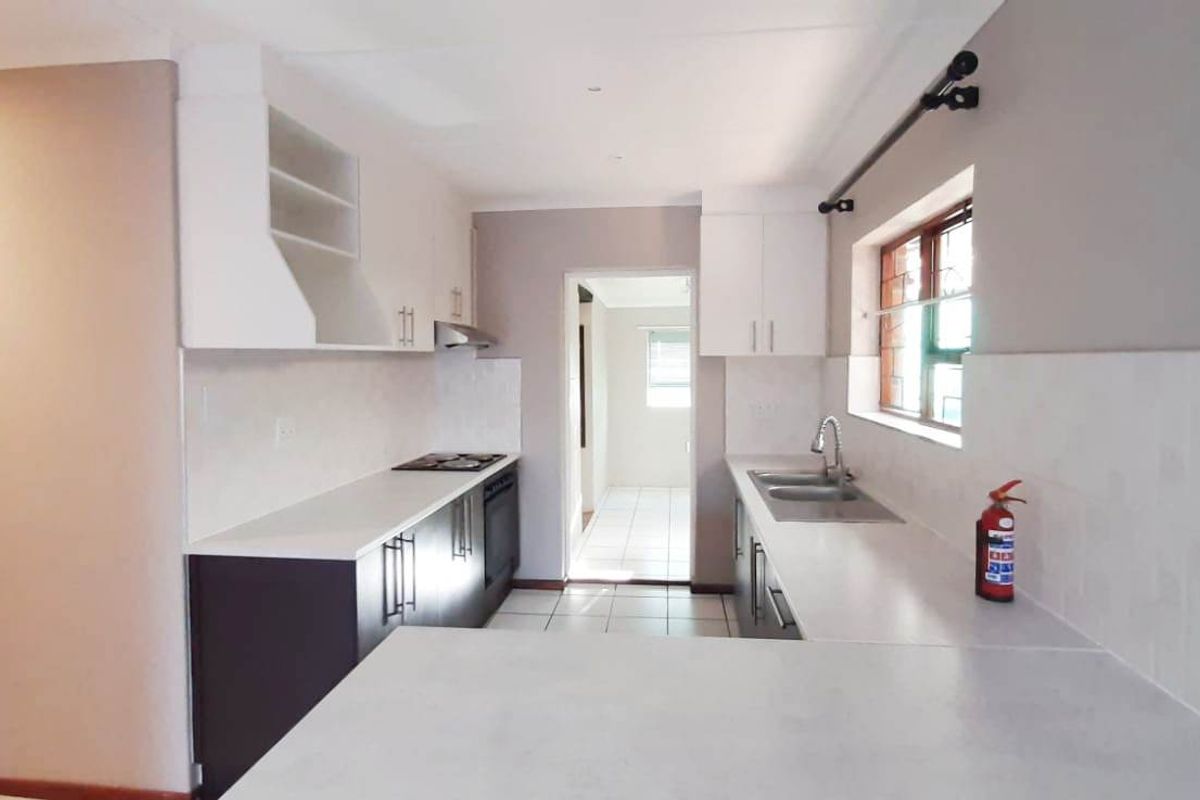 A clean, modern kitchen featuring white cabinetry, stone countertops, built-in oven and hob, and tiled flooring, offering a functional and bright workspace.