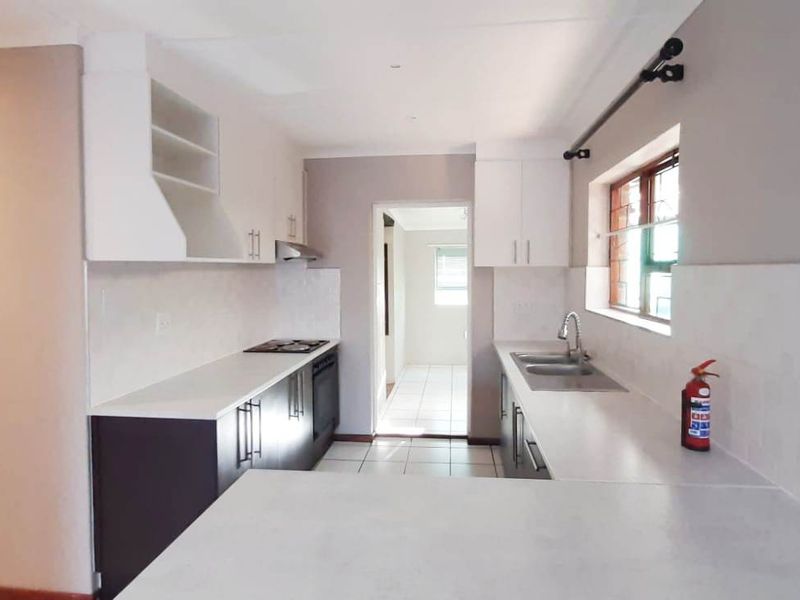 A clean, modern kitchen featuring white cabinetry, stone countertops, built-in oven and hob, and tiled flooring, offering a functional and bright workspace.