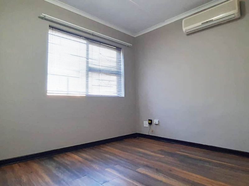 A clean, empty bedroom featuring laminate flooring, built-in cupboards, venetian blinds, and a wall-mounted air conditioning unit.