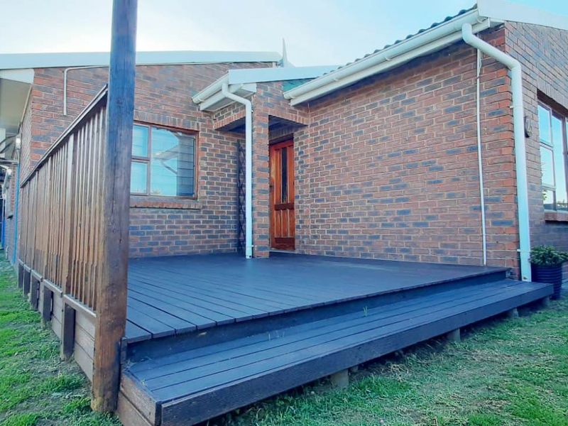 Rear view of a face brick house featuring a raised timber deck and wooden entrance door, set within a private garden area.