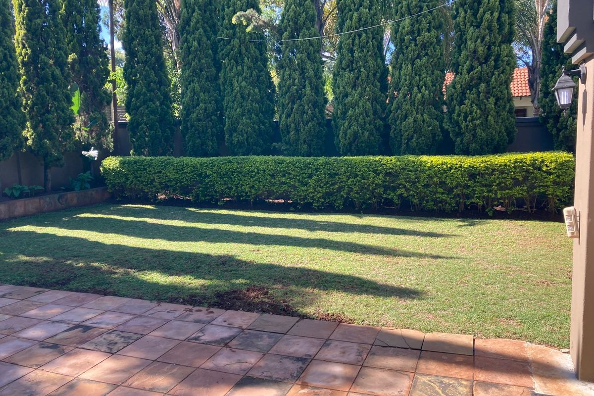 A private rear garden featuring a paved patio area, well-maintained lawn, and established perimeter hedging providing privacy.