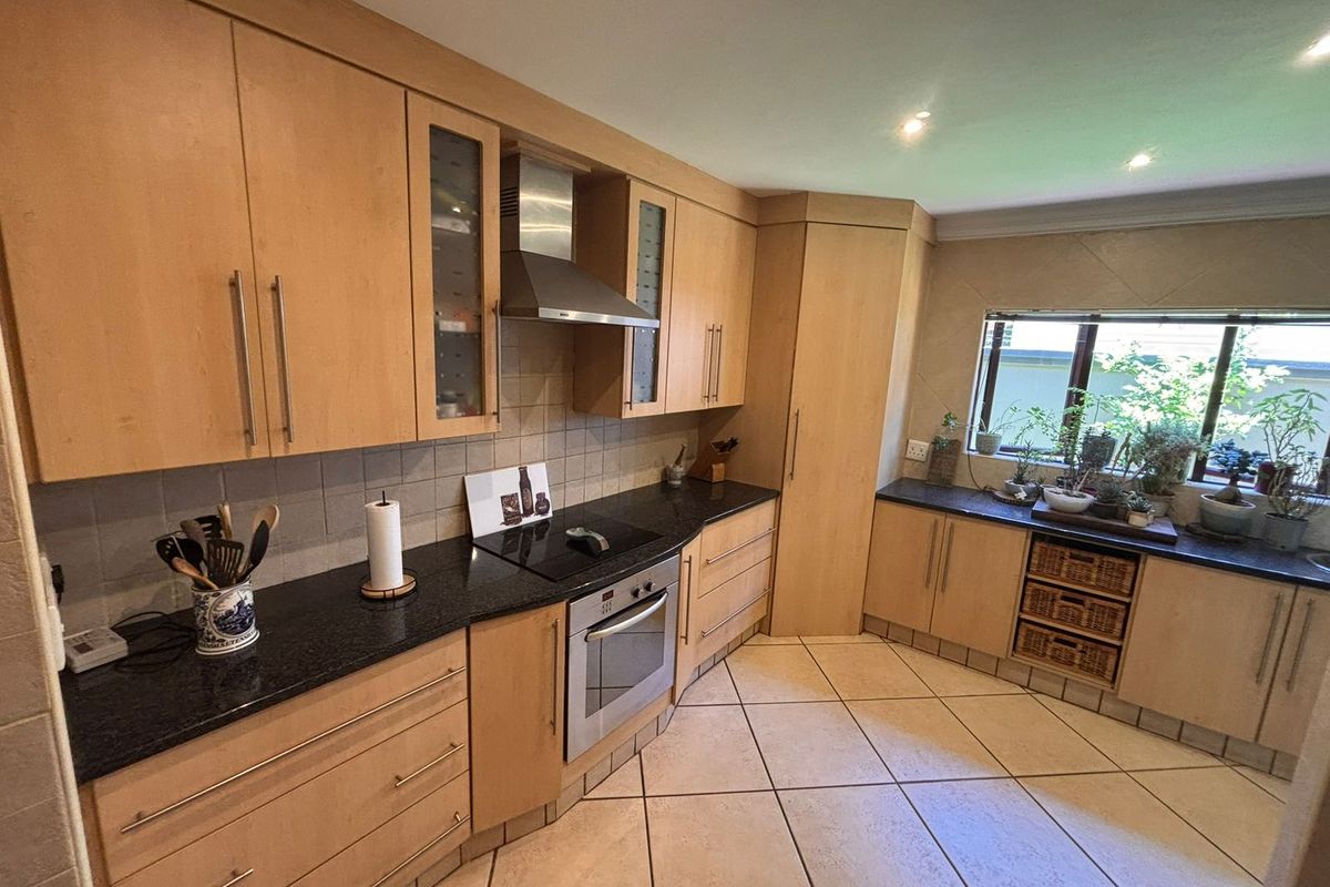 A functional kitchen featuring light wood cabinetry, dark granite countertops, integrated appliances, and tiled flooring with a neutral backsplash.
