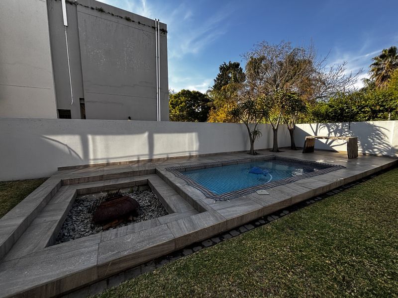 Outdoor entertainment area featuring a swimming pool with safety net, a sunken fire pit, and tiled surround set within a private garden.