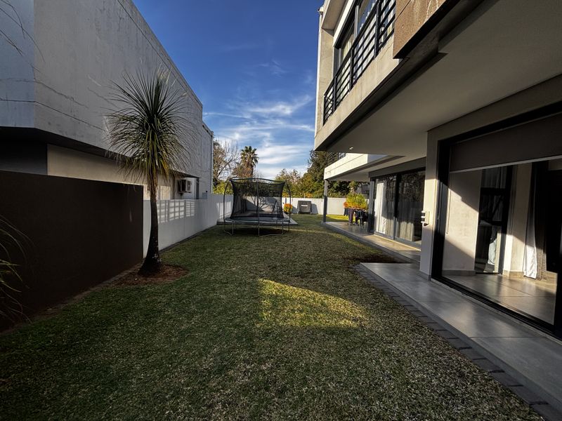 A well-maintained rear garden featuring a tiled patio area, manicured lawn, and modern sliding glass doors leading into the home.