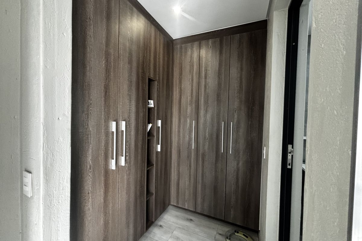 A clean bedroom area featuring modern wood-finish built-in cupboards with integrated shelving and light-toned laminate flooring.