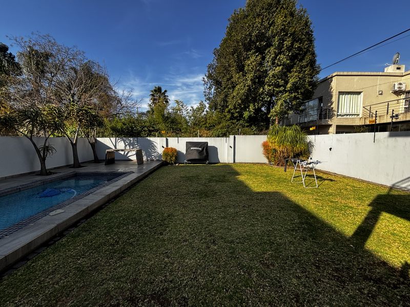 A private rear garden featuring a swimming pool with paved surround, a well-maintained lawn, and high perimeter walls for privacy.