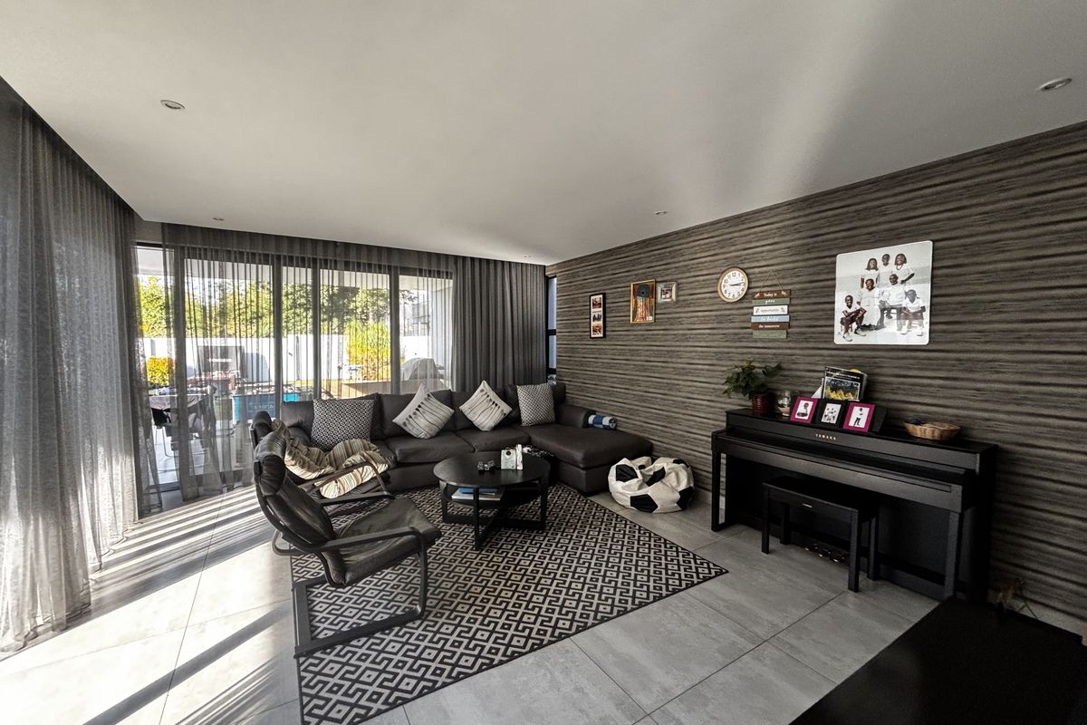 Spacious living room featuring large sliding glass doors, modern tiled flooring, and a textured feature wall, providing ample natural light and a contemporary feel.