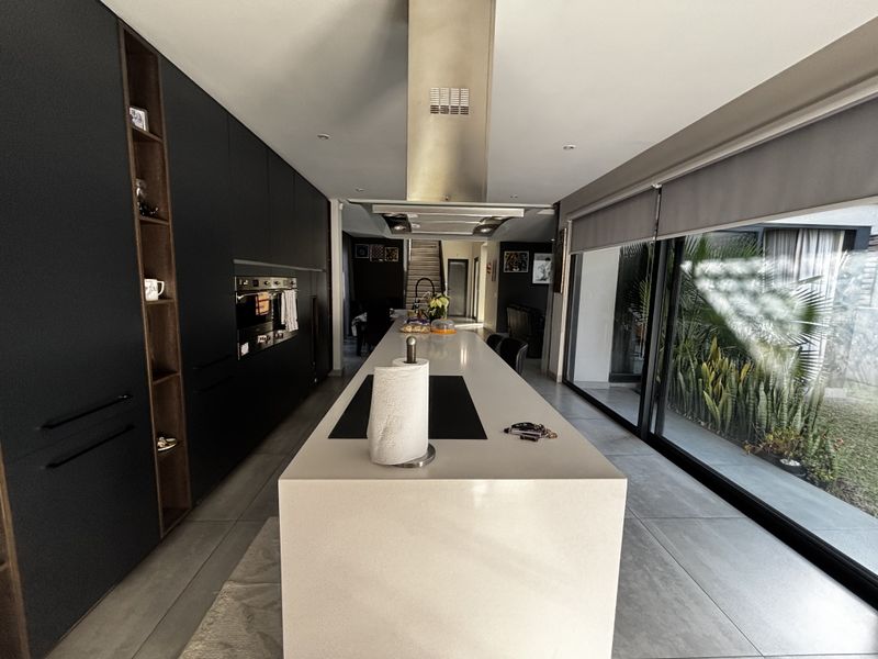 Modern kitchen featuring sleek dark cabinetry, a large central island with stone countertop, built-in appliances, and expansive sliding glass doors opening to the garden.