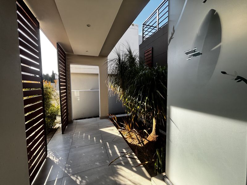 A modern, covered patio area featuring large format floor tiles, slatted timber privacy screens, and recessed lighting, creating a sleek outdoor transition space.