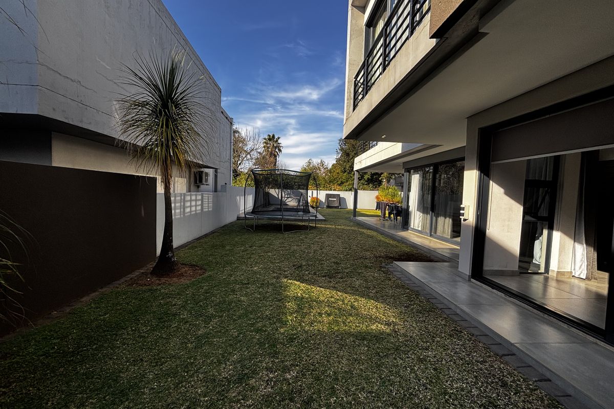 A well-maintained rear garden featuring a tiled patio area, manicured lawn, and modern sliding glass doors leading into the home.