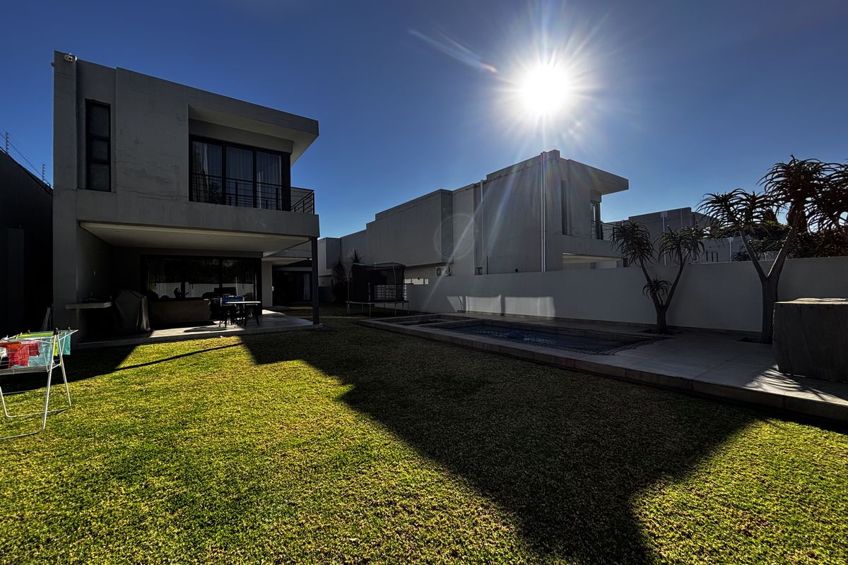 Rear view of a modern cluster home featuring a private swimming pool, manicured lawn, and a covered patio area.