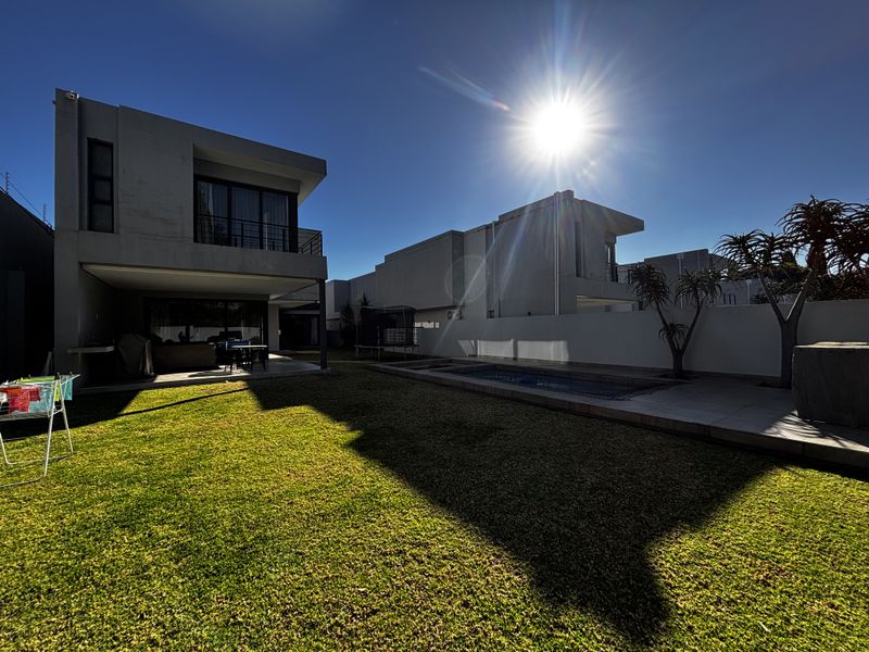 Rear view of a modern cluster home featuring a private swimming pool, manicured lawn, and a covered patio area.