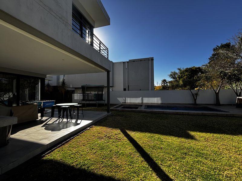 Rear view of the property featuring a covered patio, tiled outdoor area, swimming pool, and a well-maintained garden with boundary walls.