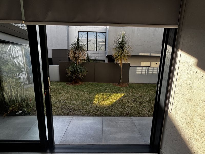 A view from an interior space through large sliding glass doors onto a private paved patio and small landscaped garden area.