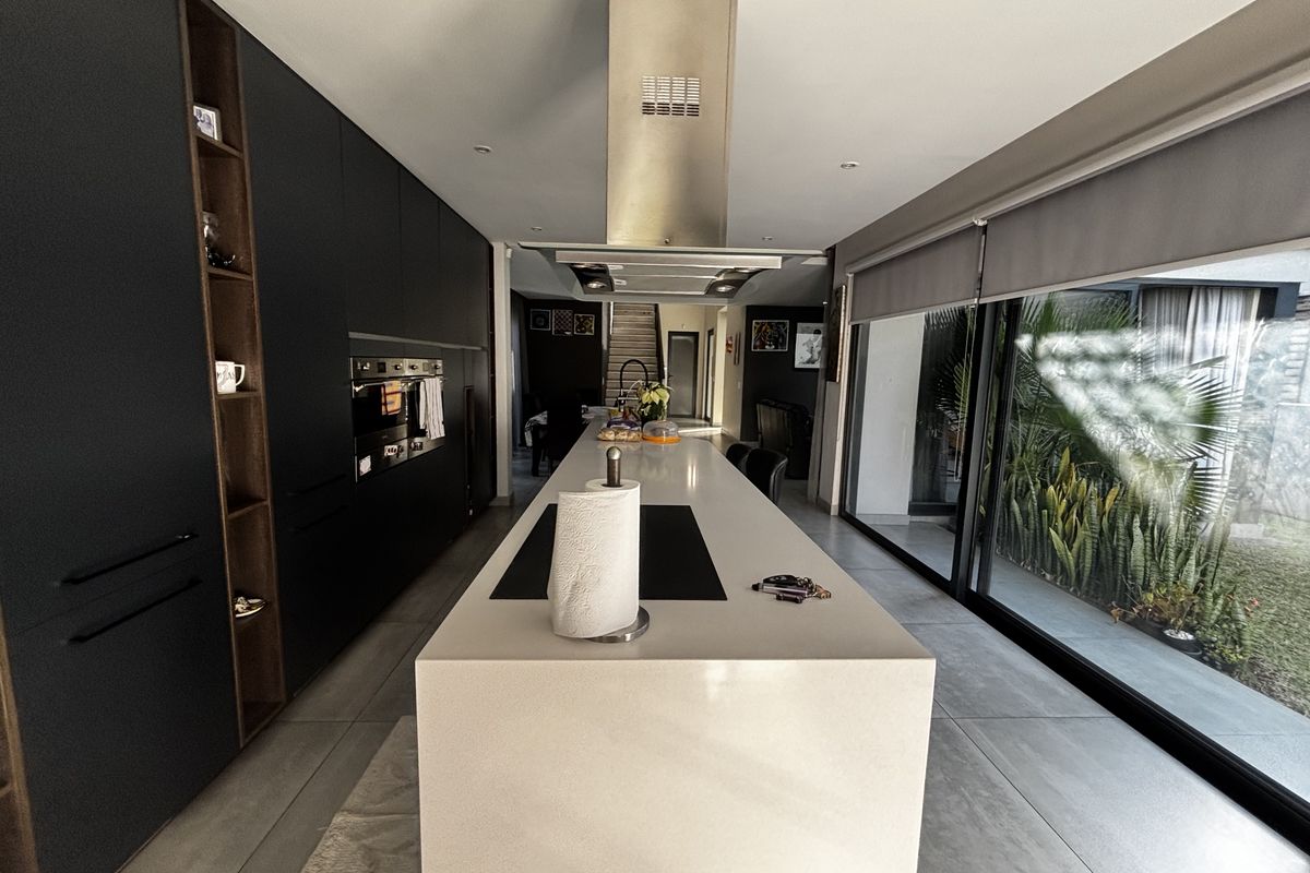Modern kitchen featuring sleek dark cabinetry, a large central island with stone countertop, built-in appliances, and expansive sliding glass doors opening to the garden.
