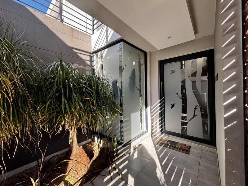 Modern entrance area featuring a stylish frosted glass front door with decorative tree motifs, tiled flooring, and a covered porch.