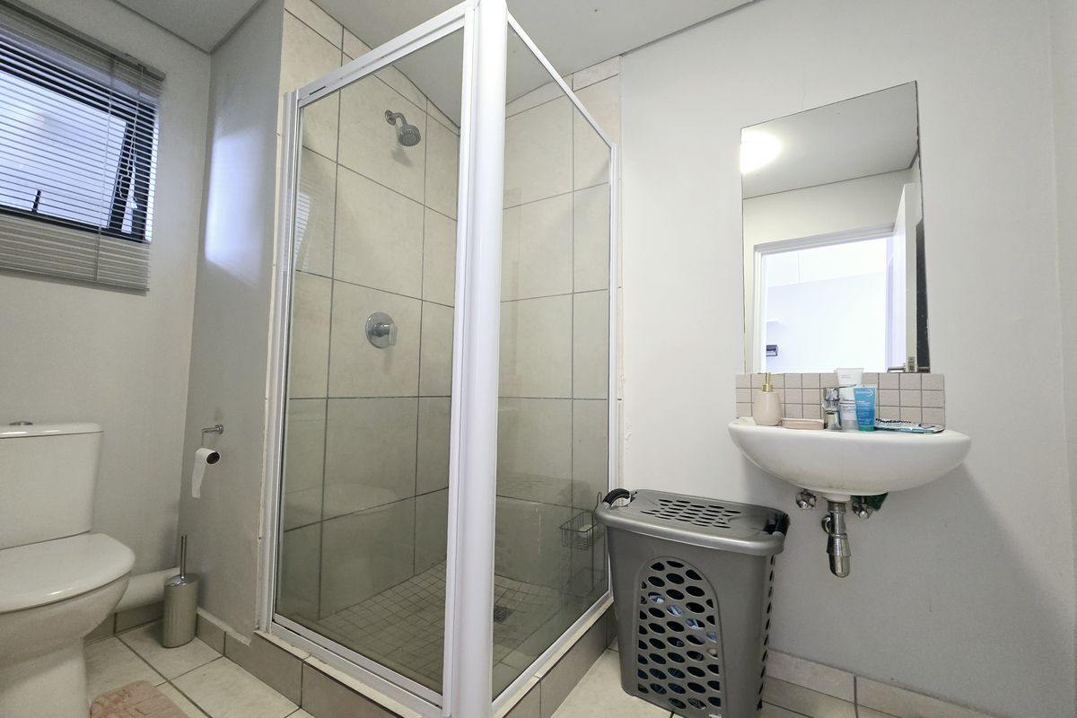 A functional bathroom featuring a corner shower enclosure, wall-mounted basin, and toilet with neutral tiled finishes.