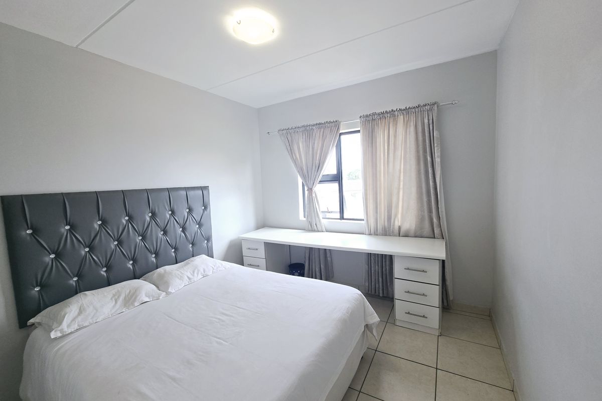 A functional bedroom featuring tiled flooring, a built-in desk with storage drawers, and a neutral color palette.