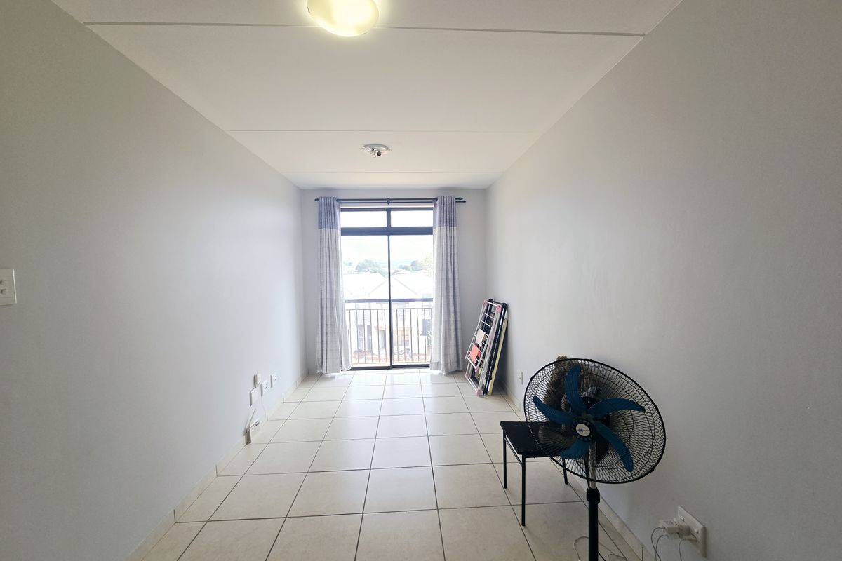 A bright, empty living area featuring neutral tiled flooring and a sliding glass door leading to a balcony, providing ample natural light.